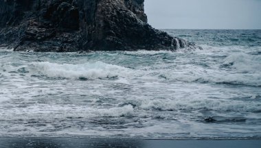 Kasvetli havalarda fırtınalı okyanusların ortasında dramatik siyah volkanik bazalt oluşumlar ve kayalar.