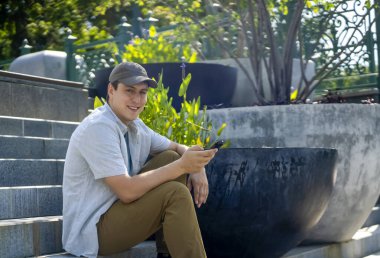 Neşeli, gülen yüzlü genç bir adam güneşli bir günde parkta telefonla konuşuyor. Başarılı bir adam akıllı bir telefonla arkadaşlarıyla iletişim kuruyor. İş, proje ya da ders çalışıyor..