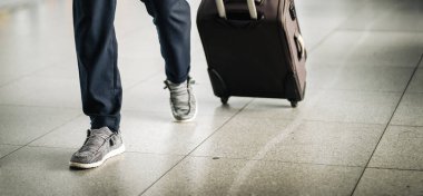 Bagajlı adam havaalanı koridoru boyunca yürüyor. İş için seyahat eden iş adamı, bavul ve bacakları yakından görüyor..