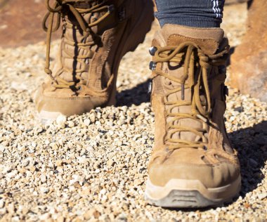 Uzun bacaklı çakal çizmeleri ve desenli taban tabanı olan bir kız, dağlarda bir patika boyunca yürüyor. Aktif bir eğlence için rahat ayakkabılar giymiş kayalık bir arazi..
