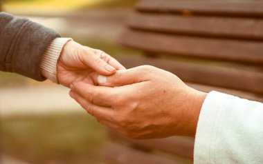 A man holds a womans hand, carefully supports a loved one, an elderly couple, husband and wife, help each other, hands with wrinkles closeup.