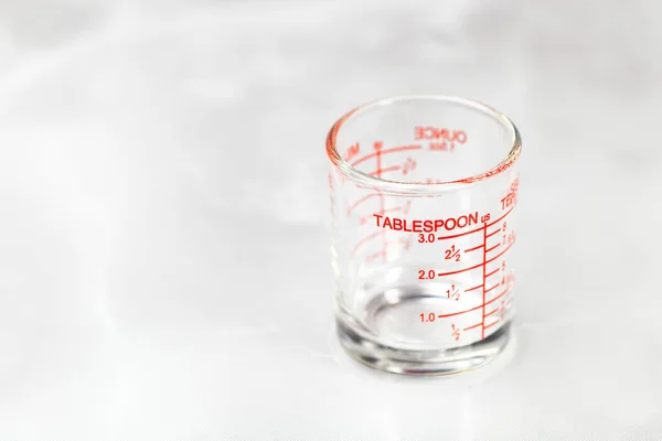 glass measuring cup or dosage cup with tablespoon measurements displayed.