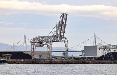 Large crane works on large coal stockpile and container at Industrial port. Cargo transportation and activity at modern shipping container terminal.