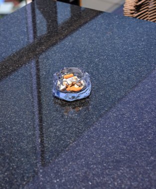 Sigara izmaritleri ve küller siyah granit masada camdan yapılmış bir kül tablasında..