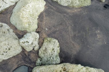 Sanur sahilinde siyah kum ve beyaz kum karışıyor ve kenarlarında kayalar. Kum ve kaya arka planı. Kum ve taş dokusu