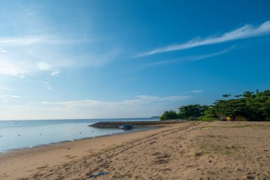 Sabahın kumsalının manzara manzarası. Deniz, beyaz kum, ağaçlar, sahil evi, küçük tekne, bulut ve açık gökyüzü var. Tanjung Benoa Sahili, Bali. Negatif boşluk