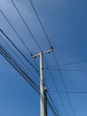 Elektrik direkleri ve kablolar, parlak mavi bir gökyüzü arka planına karşı geçiyor..