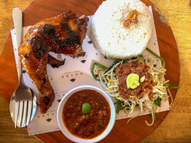 Denpasar, Bali, Endonezya (21 Mart 2021) Endonezya 'dan yerel gıda. Acı soslu ızgara tavuk, fasulye filizi ve pilav. Tahta tepside servis edilir.