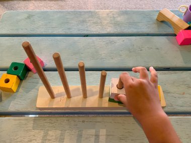 Toddler, tahta bulmaca istifleme kulesi oynuyor. Çocukların eğitici oyuncakları. Blok halka fırlatma yap-bozu. Tahta bulmaca istifleme kulesi. Yürümeye başlayan çocuğun eli bloğa sopayla girmek için oynuyor.