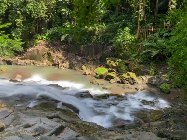 Suyun uzun pozlu görüntüsü ormanın ortasındaki kayaların arasından akar..