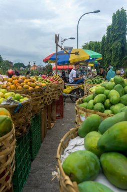 Denpasar, Bali, Endonezya (19 Haziran 2021): Denpasar 'da Pasar Kumbasari adlı geleneksel bir pazardaki tezgahlardan biri. Taze meyveyle dolu raflarla ve onlara bakan adamla dolu.