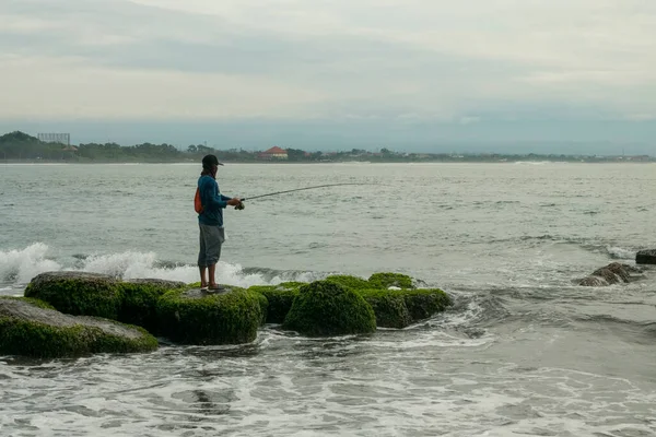 Sanur Sahili, Bali, Endonezya (20 Şubat 2021): Sanur sahilinin sabah atmosferi, dalgalar ve kayalarla dolu ve balık tutan bir adam