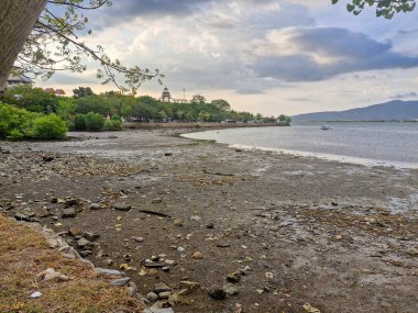 view of receding beach with cloudy sky and mountains in the background clipart