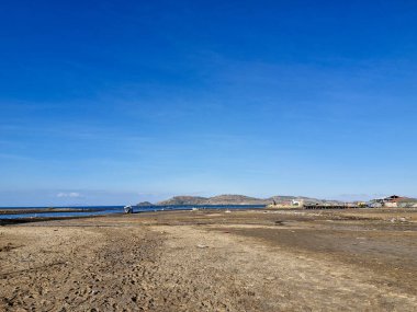 Dağınık enkazlarla, kırsal evlerle ve berrak mavi gökyüzünün altında bir su kulesiyle kuru kıyı manzarası.