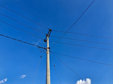 Açık bir gökyüzüne uzanan çoklu kablolu elektrik direği, bağlantıyı ve modern altyapıyı sembolize ediyor.