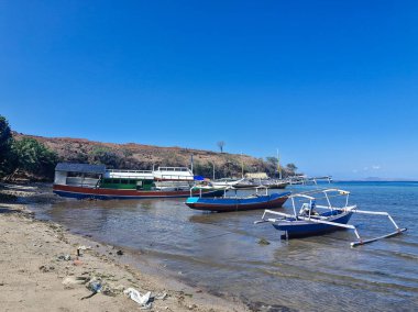 Geleneksel balıkçı tekneleri sığ kıyı sularına yanaşır, parlak mavi gökyüzünün altında mangrov ağaçlarıyla çevrilidir..