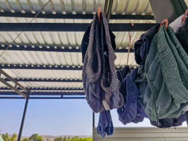 Çatı katındaki çamaşır ipinde kuruyan iç çamaşırlarının yakın çekimi. Arka planda temiz bir gökyüzü ve metal çatı yapısı var.