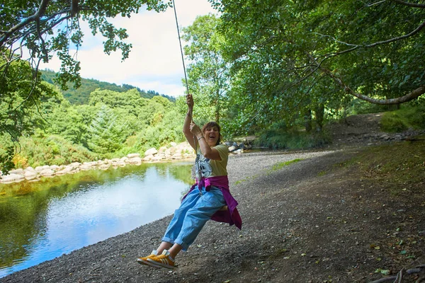Jump into the water. A woman is resting on the lake. A swing from a rope and a stick. Active recreation in nature. Summer fun. A man is riding a swing.