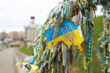 Sarı ve mavi kurdeleler Ukrayna 'da ölen Bölgesel Savunma Kahramanları onuruna verilen Ukrayna bayrağını sembolize etmektedir. Arkaplanda Bağımsızlık Meydanı