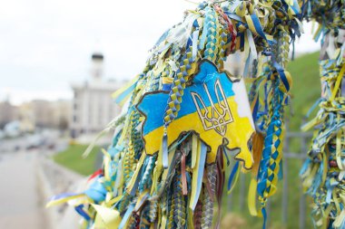 Sarı ve mavi kurdeleler Ukrayna 'da ölen Bölgesel Savunma Kahramanları onuruna verilen Ukrayna bayrağını sembolize etmektedir. Arkaplanda Bağımsızlık Meydanı