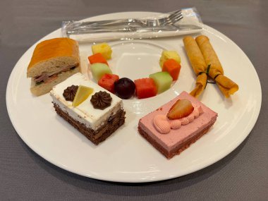 Bread, cakes and fruit are arranged on plates for meeting snacks.