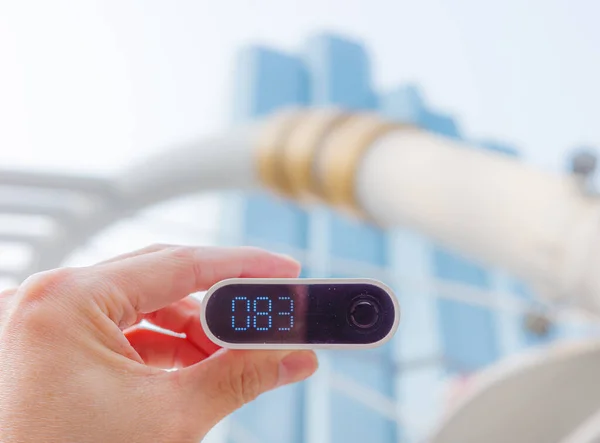 Hand holding air quality meter outdoor to see PM 2.5 level with blurry background of blue edifice in downtown of Bangkok, Thailand.