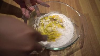 Bir kadının eli kaşıkla ve tabakta bıçakla bir kasede pasta yapıyor.