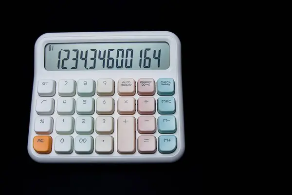 Yeşil ve pembe tuş takımlı bir hesap makinesi. Hesap makinesi siyah arkaplanda. Hesap makinesi küçük, beyaz ve renkli bir cihazdır.