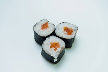 Beyaz arka planda üç somon balıklı suşi Nori 'yi sarıyor..