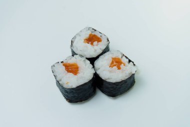 Beyaz arka planda üç somon balıklı suşi Nori 'yi sarıyor..