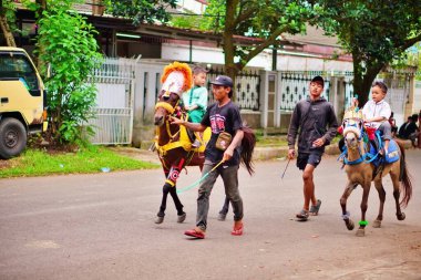 İdareciler tarafından yönetilen bir sokakta süslü midilli süren iki çocuk..