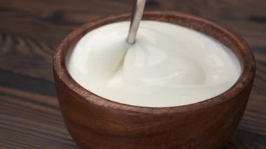 Yakın plan kaşık ve ahşap kaseden alınmış yoğurt, taze ve kremalı tatlı, ticari amaçlı konsept video.