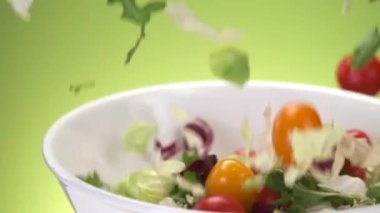 Marul yaprakları ve taze kesilmiş sebzeler yavaş çekimde kaseye düşüyorlar, ticari video konsepti.