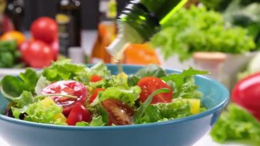 Şişeden zeytinyağı serpilmiş salata, modern mutfak arka planında taze yapraklar ve domatesler, ticari amaçlı konsept video.