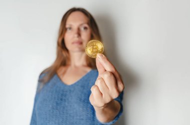 Elinde Bitcoin olan neşeli kadın mavi kazak giyen yeni dijital kripto para birimine dikkat ediyor. Beyaz arka planda izole edilmiş kapalı stüdyo görüntüleri