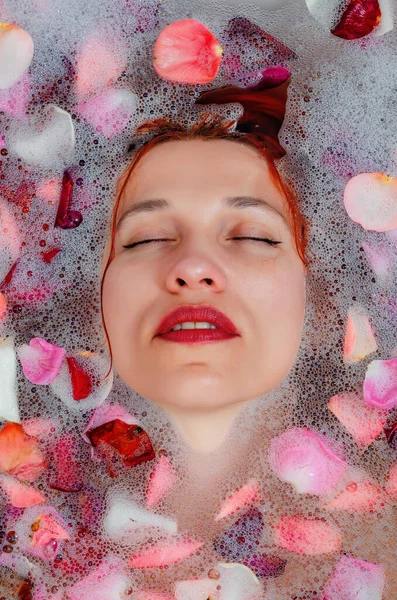 用柔和的白色 发亮的玫瑰花瓣把女性的脸贴在浴缸里 用于广告的复制空间 健美的概念 泡沫中的吸引性高加索模型 — 图库照片