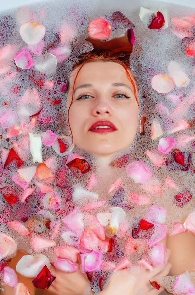 在泡沫和玫瑰花瓣之间的浴室里 一个漂亮女人的脸 — 图库照片