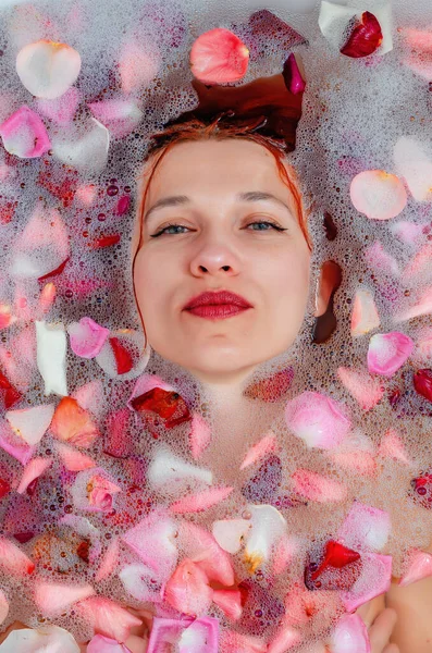 泡とバラの花びらの間の浴室の美しい女性の顔 — ストック写真