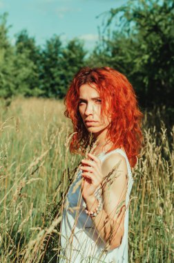 Uzun otların arasında beyaz gömlekli bir kızın romantik portresi.