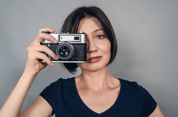 Porter of  woman with short black hair holding a camera with one hand. Smiling looking at camera.