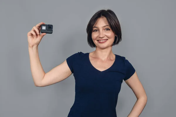 Porter of  woman with short black hair holding a camera with one hand. Smiling looking at camera. Gopro. Action camera.