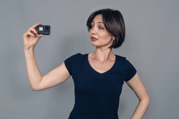 Porter of  woman with short black hair holding a camera with one hand. Head is turned to  side. Gopro. Action camera