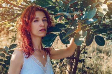 Portrait of a red-haired young girl among the trees in the garden
