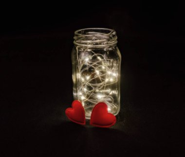 Warmth of two hearts. Atmospheric photo of glowing red hearts in glass. Black background