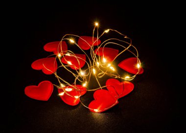 Red hearts scattered on black fabric glow. Celebration of Saint Valentine. Postcard.