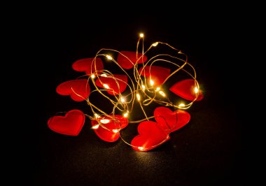 Red hearts scattered on black fabric glow. Celebration of Saint Valentine. Postcard.