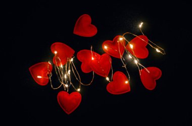Magical glow of red hearts on black fabric. View from above.