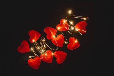 Magical glow of red hearts on black fabric. View from above.