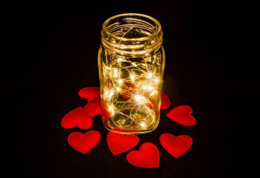 Atmospheric photo of glowing red hearts in glass. Black background