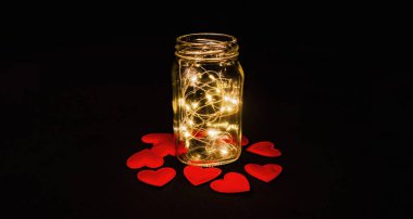 Magical glow in the glass. Red hearts on black fabric. View from above.